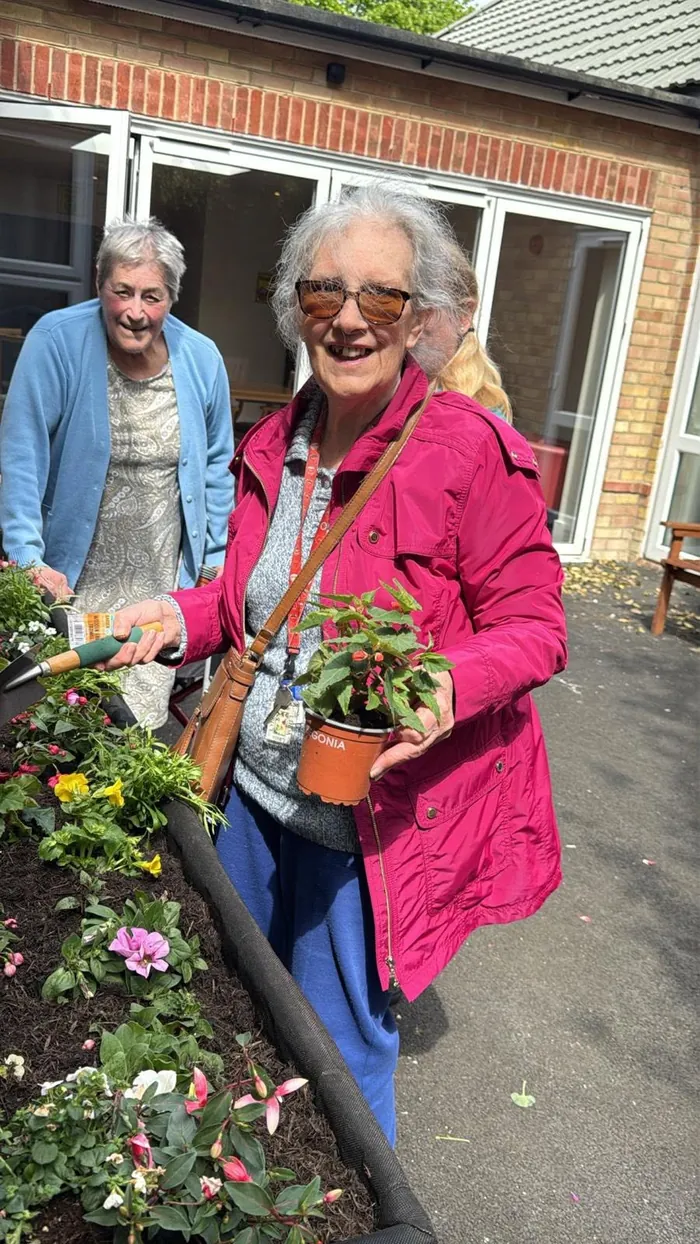 A resident in sunglasses smiling as she holds a potted plant beside the raised flower beds