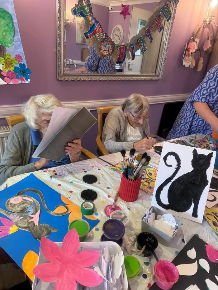 Residents painting together, with a painting of a black cat on the table